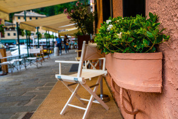 Wooden tables near traditional Italian cafe in Portofino town, Italy. Old cozy street with summer flowers. A fishing and resort town on Italian Riviera southeast of Genoa in the province of Liguria.