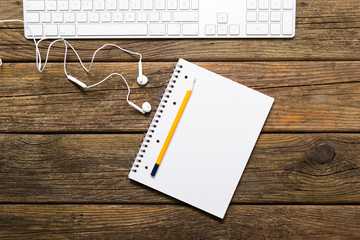 keyboard, note pad, earphones on rustic wooden table background, top view