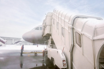 Jet bridge and white airplane parked on airport ground with airline staff and winter blue sky background.