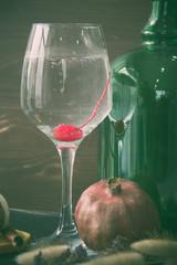 Still life of a glass with a cocktail with a cherry. Pomegranate and green bottle on a dark background