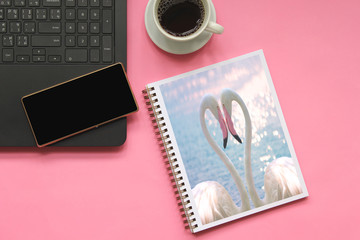 Naklejka premium Top view of flamingos making a heart shape in a books with smartphone on laptop computer and cup of coffee on pink background