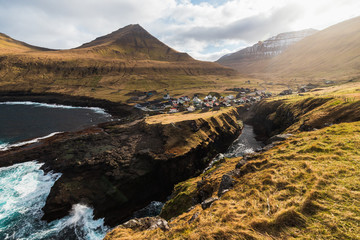 Panoramic view onto the gorge / natural harbour in Gjógv with waves hitting the cliffs and the sun in the background (Faroe Islands, Denmark, Europe)