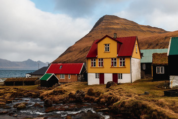 Colourful wooden houses next to a small water stream in the picturesque village of Gjógv during a...