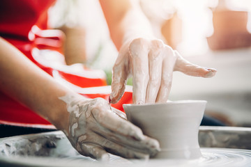 Young woman in red apron works behind potter wheel with length, making handmade plate. Concept of concentration, creativity hand