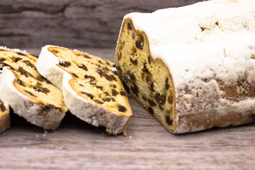 The three slices and the main part of Stollen on a wooden background. Traditional German Christmas cake with marzipan and dried fruits.
