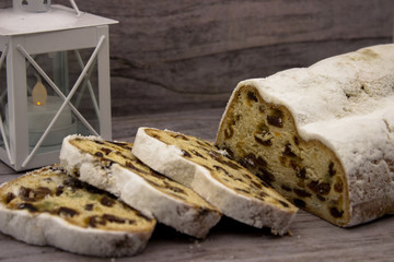 The three slices and the main part of Stollen on a wooden background. Traditional German Christmas cake with marzipan and dried fruits. In the background a white candlestick.