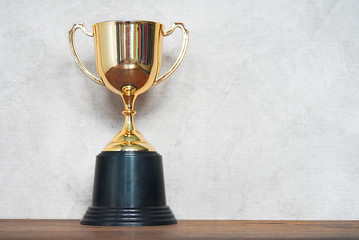 Gold trophy cup on wood table and gray background,win concept.
