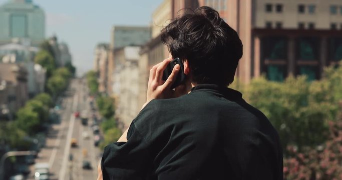 Rear view of unrecognizable man talking by smartphone in city street