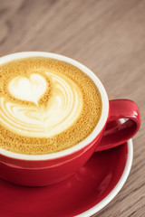 Red cup with cappuccino on a wooden table. 