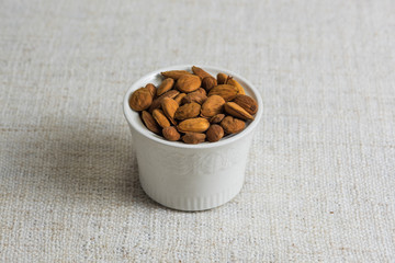 Peeled almonds in a white bowl and on beige fabric texture