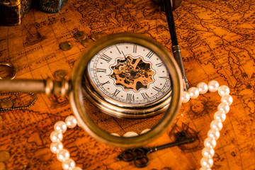 Antique clock in the background of a magnifying glass and books. Vintage style. 1565 old map of the year.