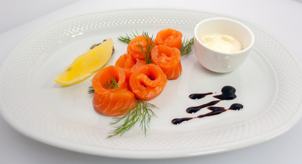 salmon rolls with lemon, capers, sour cream sauce and dill on a white plate top view