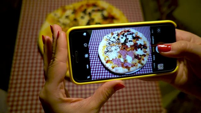 Young woman taking picture of pizza with smartphone. Woman make photo of pizza