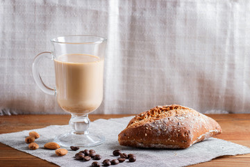 Glass cup of coffee with cream  and bun on a wooden  background and linen textile.