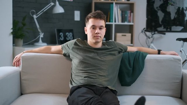 A teenage boy is resting on a couch with his legs streightened.