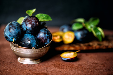 Garden plums on table. Close up of fresh plums with leaves. Summer or autumn harvest of plums. Toned image. Selective focus.