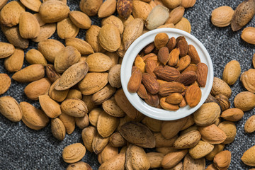 Peeled almonds in a white bowl on grey fabric texture. Nuts flat lay.