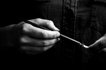 female hand elegantly holding an ink pen with a metal tip close-up on a black background. classic...