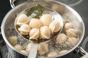 Closeup of dumplings on skimmer over stewpan with boiling water. Home cooking