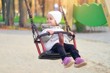 Happy child girl on swing in sunset fall. Little kid playing in the autumn on the nature park