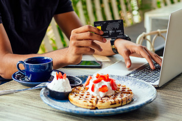 Male Customer paying for coffee and pancakes with credit card sitting with laptop online shopping black friday sale