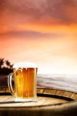 Cold fresh beer on barrel of wood. Summer sunset time. Sea landscape with beach and palms. Free space for your bottle. 