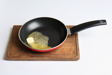 Frying pan with melting butter on board against white background