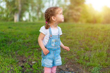 Little Caucasian girl walks on nature dressed in denim overalls