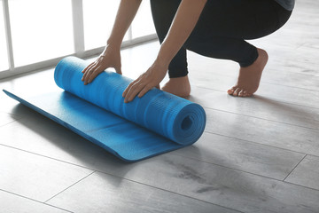 Woman rolling yoga mat on floor indoors, closeup