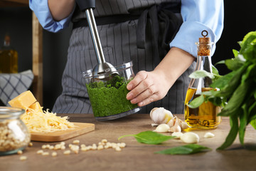Woman blending pesto sauce in bowl at table, closeup