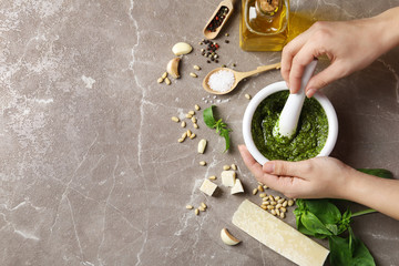 Woman mixing pesto sauce with pestle in mortar on grey table, flat lay. Space for text