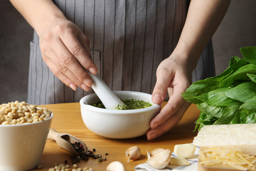 Woman mixing pesto sauce with pestle in mortar at table, closeup