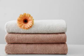 Stack of fresh towels with flower on table against white background