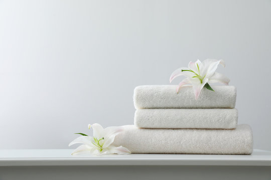 Stack of fresh towels with flowers on table against white background. Space for text