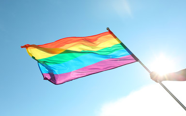 Gay man holding rainbow LGBT flag against blue sky