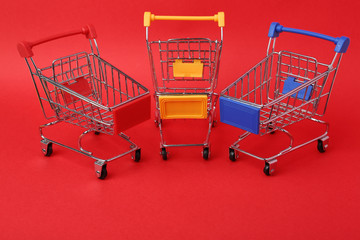 Different empty shopping trolleys on color background