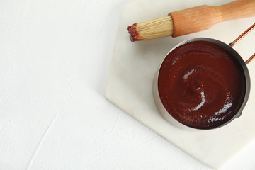 Cooking pot with barbecue sauce and brush on white background, flat lay. Space for text