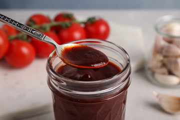 Jar and spoon with barbecue sauce on table, closeup