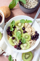 Healthy Breakfast - oatmeal porridge with kiwi,black currant,sunflower seeds and mint sprigs decorated top view in a white bowl with a spoon on a white napkin