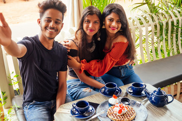 fashionable indian friends couple of two woman and man making selfie mobile phone.friends long-awaited meeting students eating pancake drinking masala tea after shopping.summer instahram lifestyle