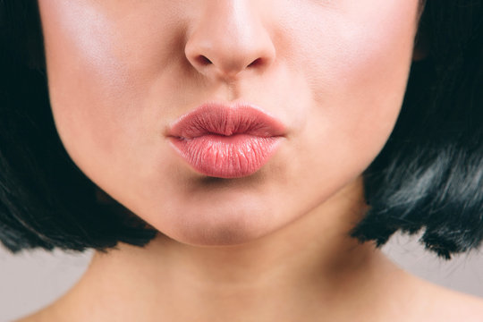 Cut view of beautiful lips with lipstick on. Young brunette with bob haircut. Kiss. Naked neck. Isolated on light studio background.