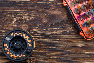 Multi-colored bait for fishing in a box and a reel for fishing rods on a wooden background