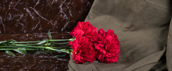 on a marble brown slab lies a bouquet of red flowers, the memory of the dead soldiers in the war