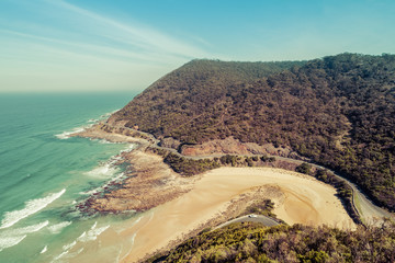 Great Ocean Road and forested hills on sunny day - aerial view