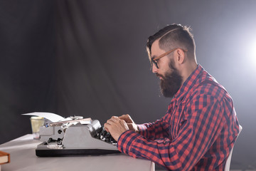 People and technology concept - Side view handsome man with beard working on typewriter over black background