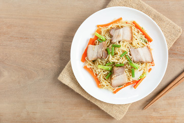 top view of stir fried egg noodles with pork belly in a ceramic dish on wooden table. asian homemade style food concept.