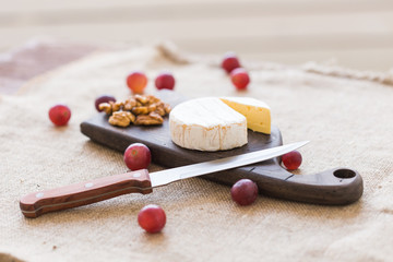 Brie or camembert cheese with nuts and grapes on a board