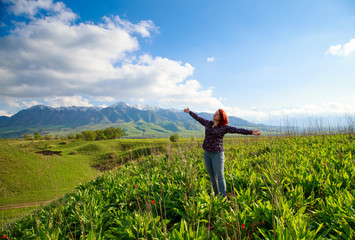 Girl on the nature with joy looks at the mountains. Beautiful summer landscape. High mountains, green hills and bright blue sky. Background and theme of travel and adventure.