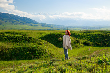Girl on the nature with joy looks at the mountains. Beautiful summer landscape. High mountains, green hills and bright blue sky. Background and theme of travel and adventure.