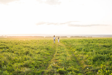 Naklejka na ściany i meble Family, summer and holiday concept - Mother holding her daughter's hand running in green field
